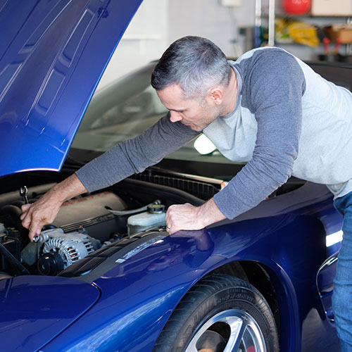 A man lovingly tends to a blue muscle car in his garage. 