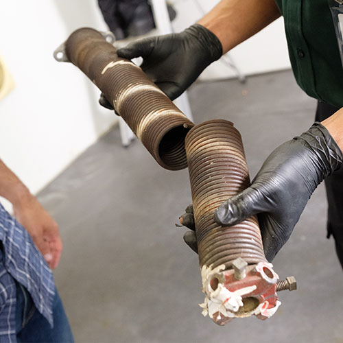 A technician shows a customer a broken spring. Precision uses high-quality parts so your garage is guaranteed to work for years.